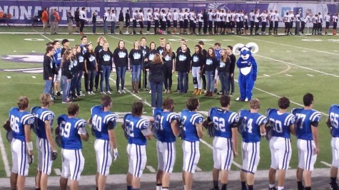 The Cotter football team lines the side of the field as the show choir sings the national anthem
