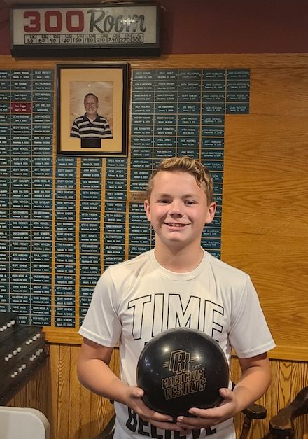 Chase Petschow poses in Westgate Bowls 300 Lounge, in the background is a photo of Vic Schewe, Winonas first 300 bowler